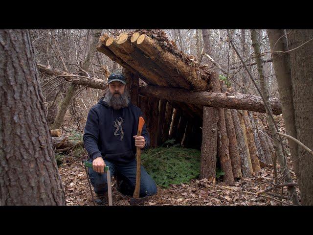 Building of a shelter under a fallen tree with campfire heating