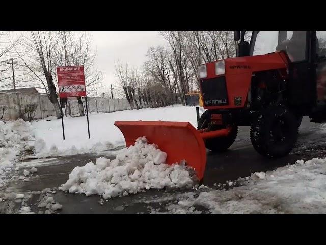 Трактор Уралец-250 с кабиной убирает снег на стадионе.