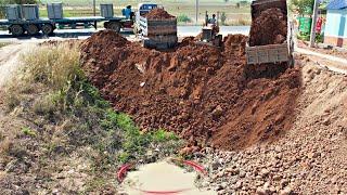 Komatsu Bulldozer pushing soil into a deep pit next the road with Dump Truck unloading