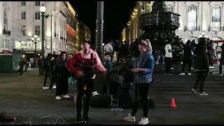 Kathie Kleff singt mit Straßenmusiker "Shallow" auf dem Piccadilly Circus in London