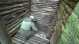 A man builds a log cabin in the forest using improvised means. Shelter