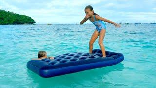 Children swim and dive in the sea on the beach with a mattress